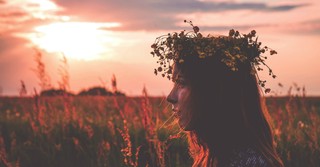 A woman in a field at sunset, wearing a flower crown