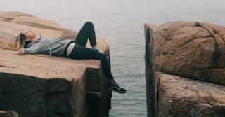 Woman lying on a cliff, listening to music