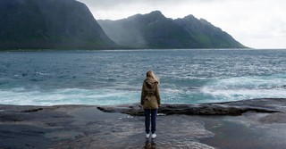 Woman standing by the sea with mountains in the distance