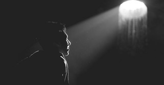 Black and white photo of a man in the dark, looking up at the light