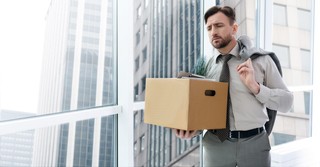 Sad man fired from his job, carrying a box out of the office