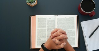 Hands folded in prayer over an open Bible