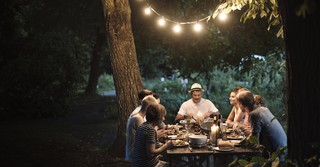 group of people sitting at table outside under string lights in the evneing