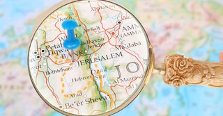 Magnifying glass over a map of Jerusalem with a push-pin in the map