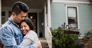 middle age Asian couple hugging outside of home and smiling