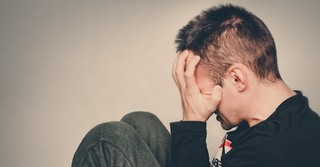 Grieving young man with knees scrunched up and hands over eyes