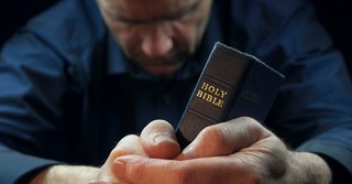 Man holding a Bible and praying over it