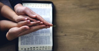 Parent and child praying over their open Bible