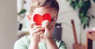 Young boy holding a paper heart in front of his face