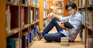 Student sitting in a library reading a stack of books