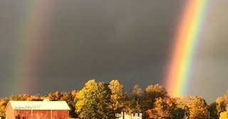 A double rainbow against a dark sky by a barn