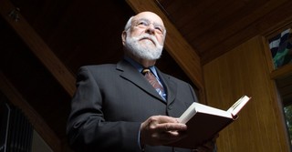 older man with glasses wearing a suit and reading bible in church