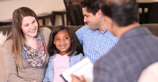 A young girl sitting with two adults, completing adoption process
