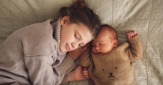 Big sister cuddled up with baby brother, taking a nap