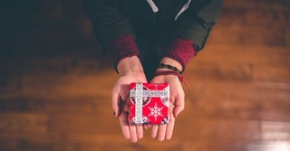 A person holding out a small Christmas gift