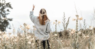 Woman in a field with of flowers with her hand raised praying