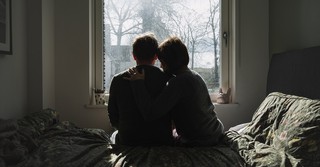 Wife comforting hugging depressed husband on bed looking out window depression