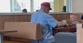 a toddler sitting with an elderly man in a McDonald's booth