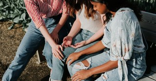 Three women sit together on a park bench, offering comfort and support as they talk and listen, illustrating friendship, encouragement, and Christian community.