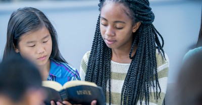 An older girl shares the Bible with a younger girl