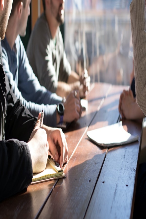 Men sitting at picnic table talking, writing. Source https://unsplash.com/photos/KdeqA3aTnBY