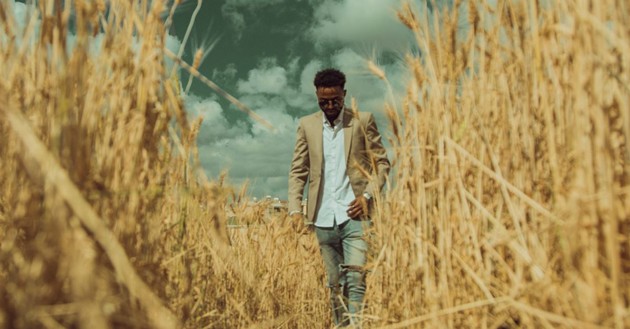 man walking through a split in a tall hayfield, sunglasses on, sunshiny day