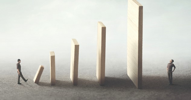 man knocking domino which will flatten man on other end blind leading the blind