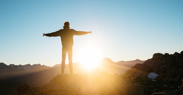 back view of man on hilltop at sunrise arms out in praise