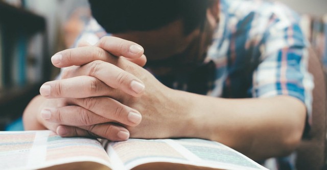 man praying with folded hands on top of bible