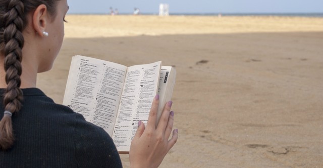 back view of a girl reading the Bible on the beach