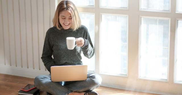Smiling woman holding a cup of coffee while working on a laptop