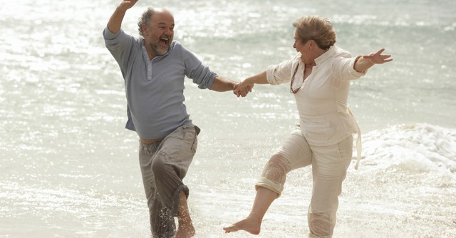 happy senior retired couple splashing and laughing at a beach