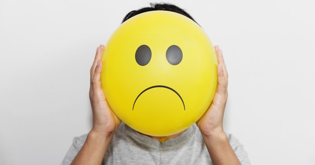 A person holding a balloon with a frowny face in front of their own face
