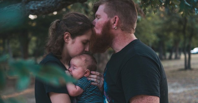 Husband kissing his wife while she holds a baby.