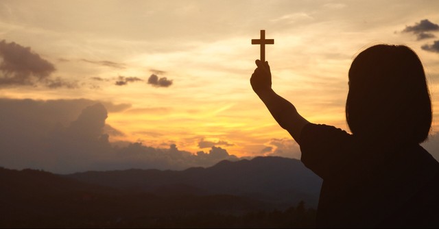Girl holding up the cross at sunset