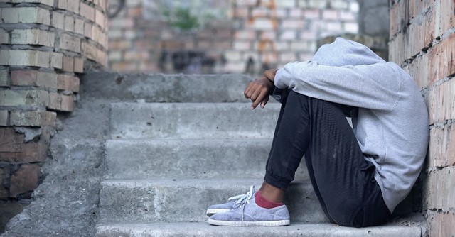 young teen boy sitting alone on steps looking in need