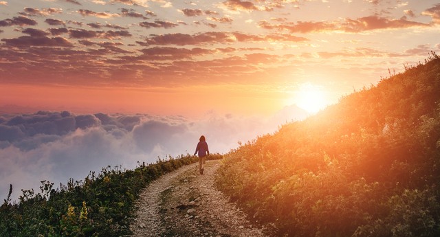 woman hiking on trail around mountian toward sunset