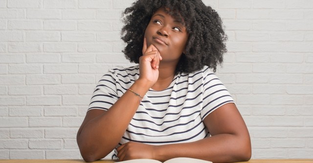 woman looking up and questioning what is in book