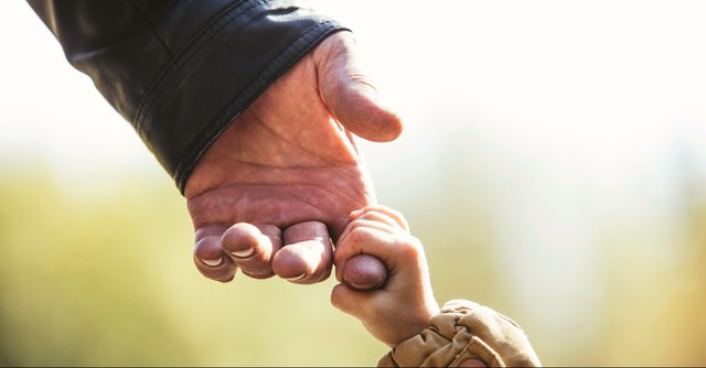 A young child's small hand holding an elderly man's finger