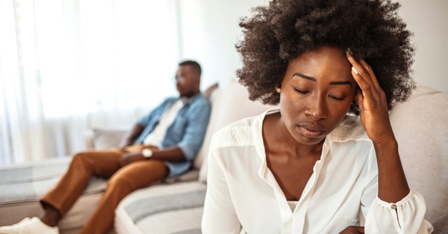 Close-up of an unhappy woman with her husband ignoring her in the background