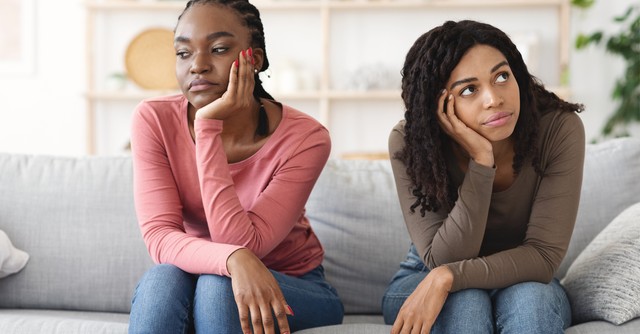 Two women sitting next to each other on a couch, looking unhappy