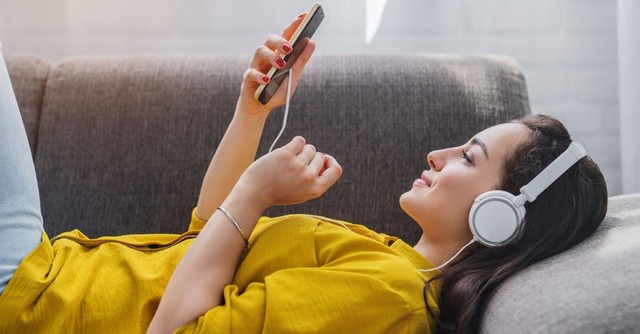 woman listening to her phone with headphones, laying down relaxing