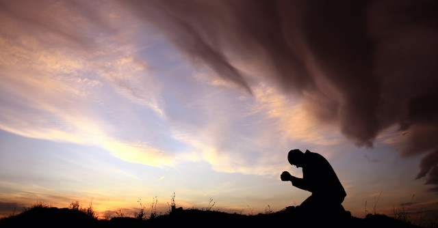 silhouette of man praying outside at dusk in a field