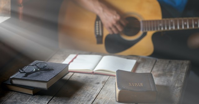 man playing guitar with journal and Bible on table