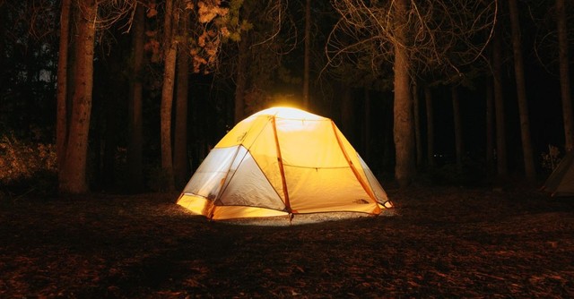 A brightly lit tent in the woods at night