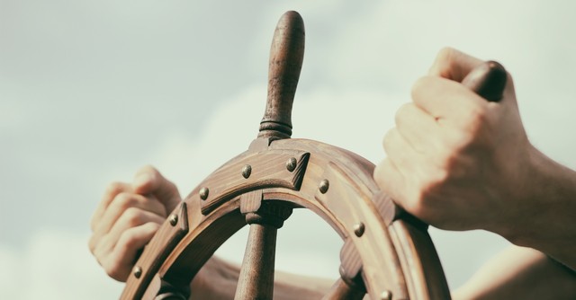 hands holding a ship's steering wheel