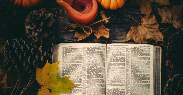 An open Bible surrounded by fall leaves, pumpkins, and candles