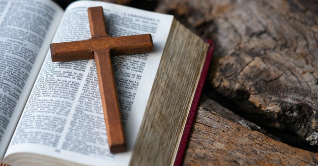 wooden cross laying on open Bible pages