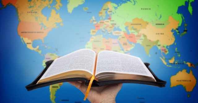 Person holding an open Bible up in front of a world map