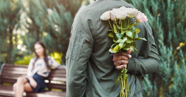 Man holding flowers behind his back to surprise a woman